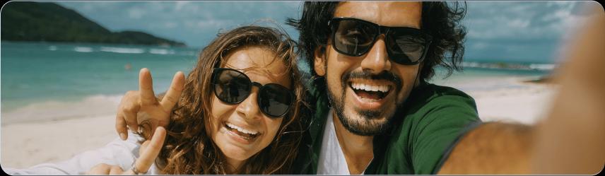 Um casal sorridente tirando uma selfie na praia.