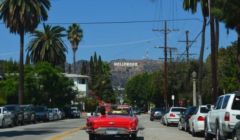 Carro vermelho na estrada rumo às montanhas com o Letreiro de Hollywood, em Los Angeles