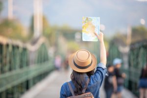 mulher de costas usando camisa jeans e chapéu erguendo um mapa em cima de uma ponte
