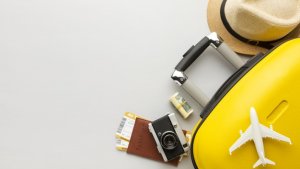 imagem de uma mala amarela, com um avião em miniatura em cima e ao lado de um chapéu e um pasaporte