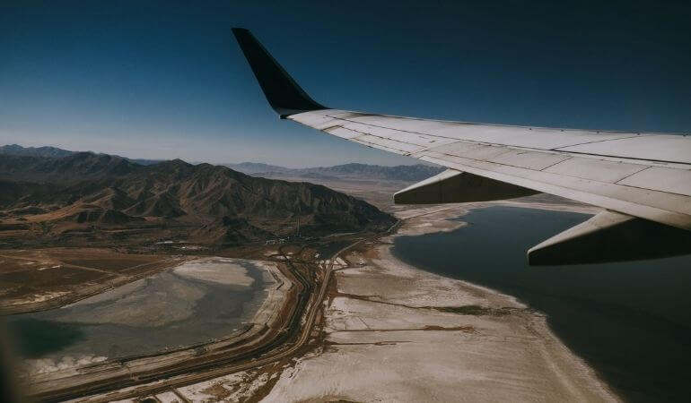 vista de dentro da janela de avião, vendo a asa dele e a cidade abaixo no horizonte
