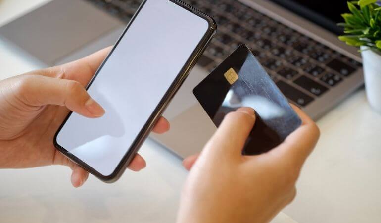 mãos femininas segurando um celular na esquerda e um cartão de crédito na direita