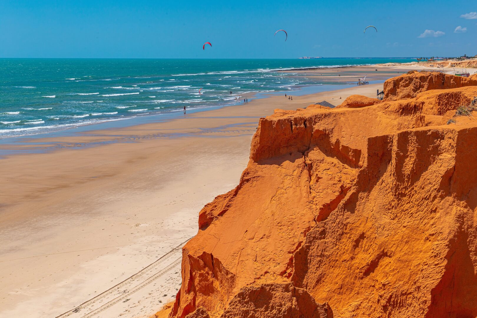 Vista de uma rocha laranja, da faixa de areia e do mar de Canoa Quebrada